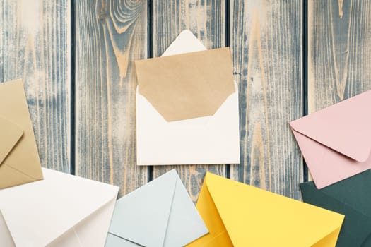 White open envelope with open kraft paper card on gray wooden background. Multicolored envelopes lie side by side. Copy space. Top view. Mail, correspondence, sending messages, congratulations