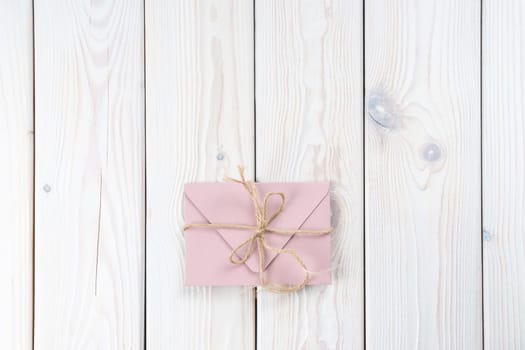 Pink envelope tied with rough jute rope on white wooden background. Copy space. Top view. Mail, correspondence, sending messages, congratulations