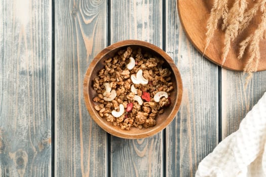 Wooden bowl filled with whole grain granola with berries and nuts. Delicious and healthy breakfast. Tray of spikelets and white towel on rustic wooden surface. Top view