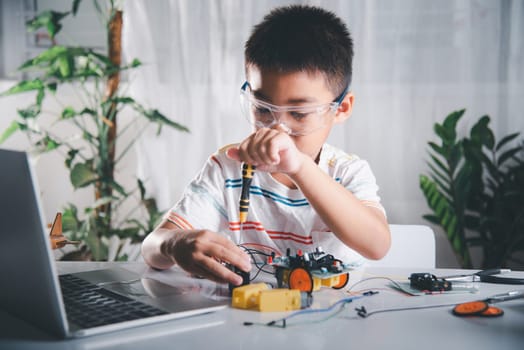 Little child tighten the nut with a screwdriver to assemble car toy, Asian kid boy assembling the Arduino robot car homework project at home, education AI technology workshop school learning lesson