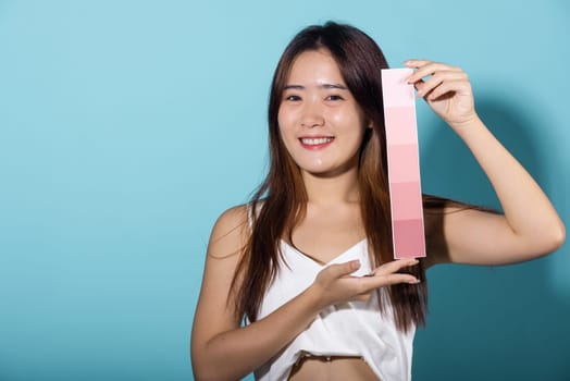 Asian beautiful young woman holding skin color scale paper studio shot isolated on blue background, Portrait of happy female hold color card under sun protection, skin beauty face