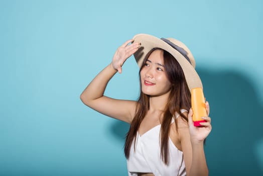 Beautiful Asian young woman holding body lotion on hand in studio shot isolated on blue background, Smiling brunette female hold cream sunblock bottle, tube of sunscreen, protect sun light and UV