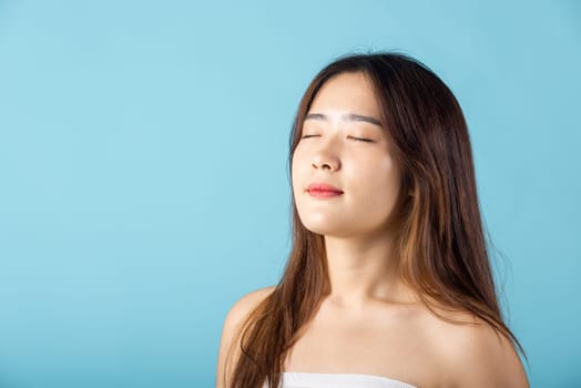 Front portrait of Asian young woman beautiful face closed eyes and smiling studio shot isolated on blue background, close up face of happy female healthy sleeping, beauty care calm and relaxed