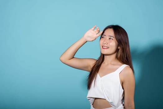 Asian young woman hand up cover face protect sun light and UV smile in studio shot isolated on blue background, female raising arm and hand in protection and block sunshine, sunscreen cream advertise