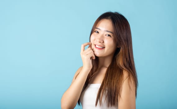 Skin care and Beauty concept. Portrait happy woman with natural makeup and healthy face studio shot isolated on blue background, Asian young female with beauty face touching healthy facial skin