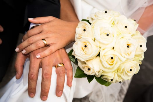 Close-up view of a bridal bouquet made of roses pale yellow and hands of the couple in the background
