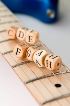 slanted detail view of the fretboard of an electric guitar with letter-wood cubes of the scale lying on the strings low depth of field