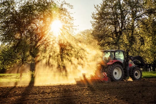 Tractor plowing a field at sunset in beautiful sunlight falling through trees and dust with light and shadow effects,no logos or faces
