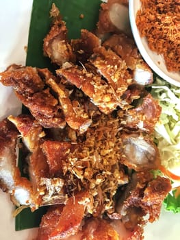 Fried pork on banana leaf in a white plate.