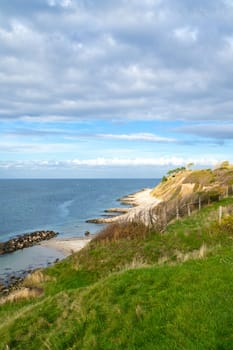 Hundested, Denmark on the cliff overlooking the sea. Baltic Sea coast, grassy meadow, beach. Clouds on horizon. Landscape photo from Scandinavia.