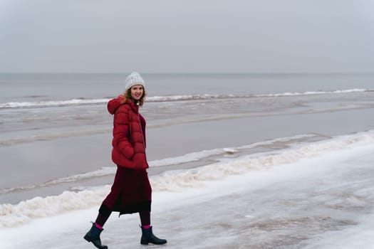 A woman in red warm clothes walks along the sea in winter.