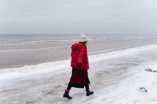 A woman in warm clothes walks along the sea in winter.