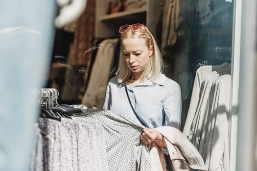 Woman shopping clothes. Female shopper looking at fashionable clothes indoors in clothing store.