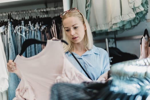 Woman shopping clothes. Female shopper looking at fashionable clothes indoors in clothing store.