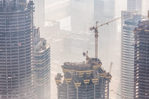 Huge skyscrappers construction site with cranes on top of buildings. Rapid urban and construction sector development or inflation of real estate bubble.