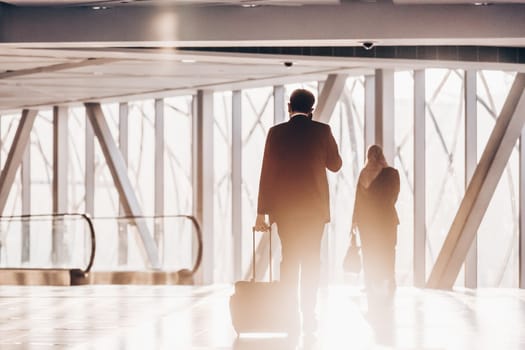 Businessman dragging a small carry on luggage suitcase at airport corridor walking to departure gates.