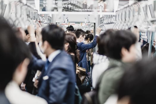 Passengers traveling by Tokyo metro. Business people commuting to work by public transport in rush hour. Shallow depth of field photo. Horizontal composition.