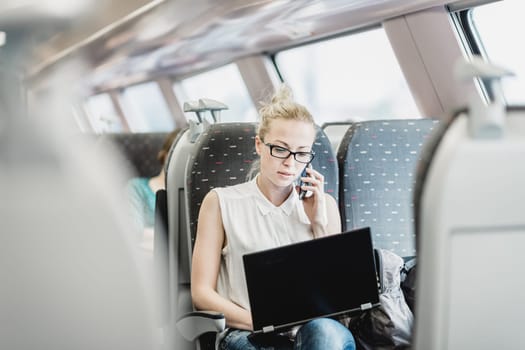 Businesswoman talking on cellphone and working on laptop while traveling by train. Business travel concept.