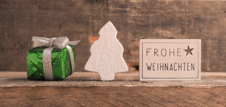 Frohe Weihnachten on a small sign, German Merry Christmas with decoration on a wooden background