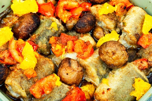 Fried hake fish grilled with orange, tomato and mushrooms. Close up