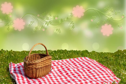 Red checked picnic blanket with empty basket on a meadow over abstract spring background. Beautiful backdrop for your product placement or montage.