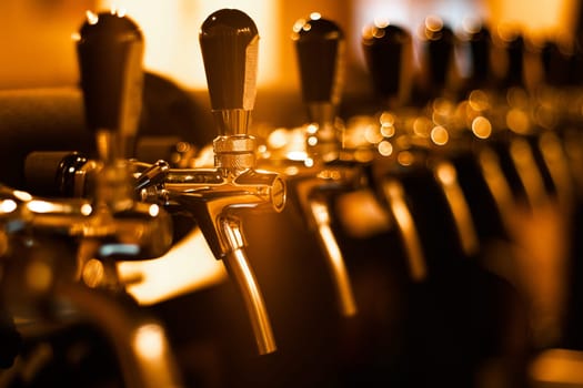 Creatively blurred image of faucets in beer pub with defocused bokeh and artistic digital noise. Golden row of taps in tap room. Bar background image