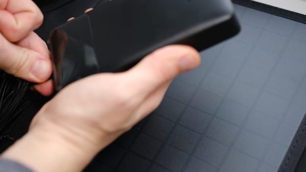 Hands plug in portable solar panel charging power bank by mutlipurpose cable, smartphone, watches, laptops. Clean energy for using in camping or at home when NO electricity
