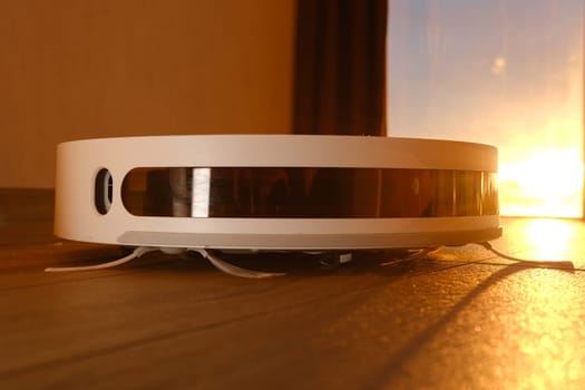 white vacuum robot cleaner close up with sunset light on the brown dalle with beautiful flares and dust around.