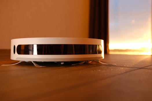 white vacuum robot cleaner close up with sunset light on the brown dalle with beautiful flares and dust around.