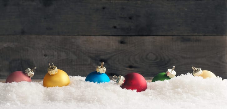 Colorful Christmas baubles in the snow, wooden background with space for text, seasonal backdrop