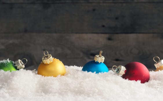 Colorful vintage Christmas baubles in the snow, wooden background with space for text, seasonal backdrop