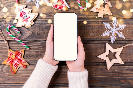 Close up woman holding phone with empty white screen mockup near decorated festive tree, celebrating Christmas, customer shopping online, purchasing gifts, browsing gadget apps