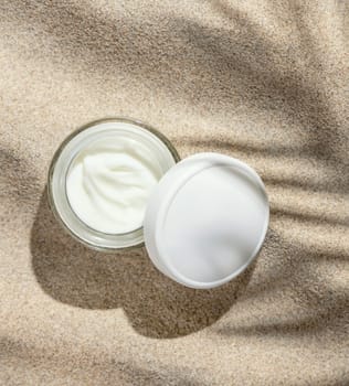 Opened Cream jar with white lid on beige sand top view. Packaging mockup. Natural skincare product for beauty. Summer sunny day with palm leaf hard shadow, tropical vacation mood