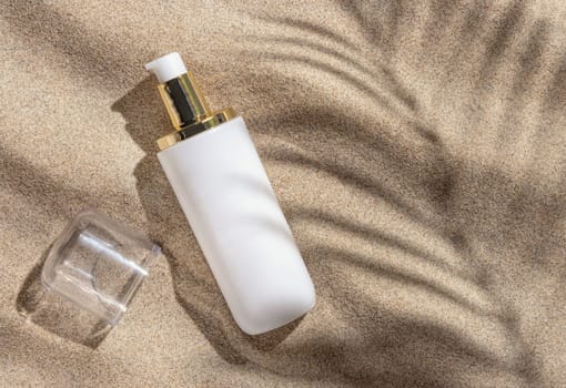 Blank white one pump cream bottle on beige sand top view. Packaging mockup. Natural skincare product for beauty routine. Summer sunny day with palm leaf hard shadow, tropical vacation mood