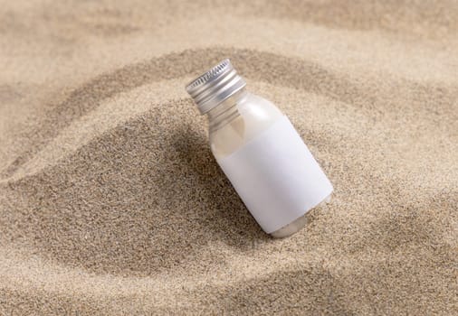 Blank Cream bottle with blank label on beige sand close up. Cosmetic packaging mockup. Natural skincare product for beauty routine. Summer tropical vacation mood