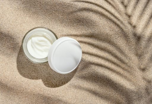 Opened Cream jar with white lid on beige sand top view. Packaging mockup. Natural skincare product for beauty. Summer sunny day with palm leaf hard shadow, tropical vacation mood