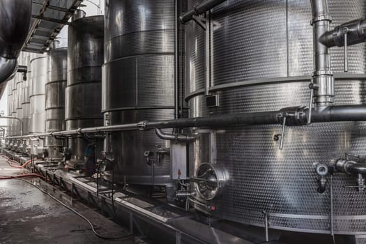 A row of steel wine tanks for wine fermentation at a modern winery. Large brewery silos typically used for storing barley or fermeted beer against blue sky.