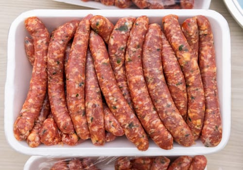 Raw sausages in a plastic tray top view. Traditional italian BBQ food during summer time. Rustic style Sausages close up