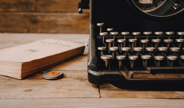 A black vintage typewriter with a rubber and an old book on wooden background.
