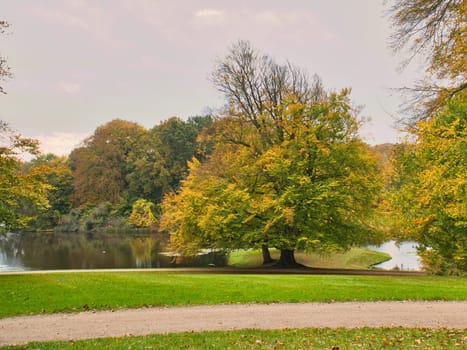 Frederiksborg Castle Park in autumn with mighty deciduous trees on the garden meadows. Colorful colors of the leaves. Walk in Denmark