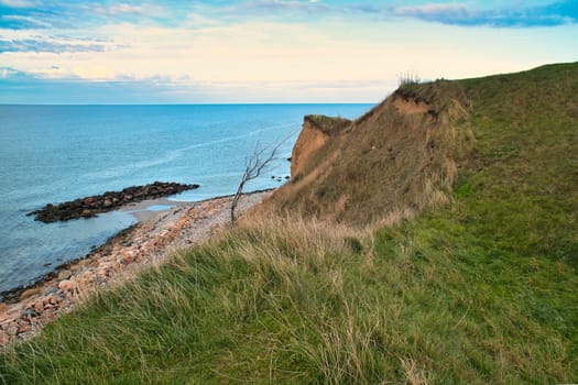 Hundested, Denmark on the cliff overlooking the sea. Baltic Sea coast, grassy meadow, beach. Clouds on horizon. Landscape photo from Scandinavia.