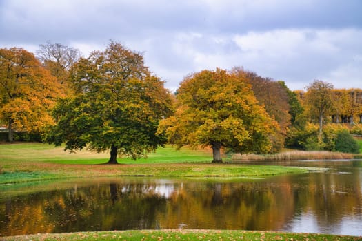 Frederiksborg Castle Park in autumn with mighty deciduous trees they are reflected in the created lake. Bright colors of the leaves. Walk in Denmark