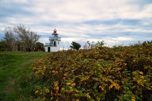 Lighthouse, Spodsbjerg Fyr in Huntsted on the coast of Denmark. Sun rays shining through the clouds. Meadow with trees. Landscape photo from sea