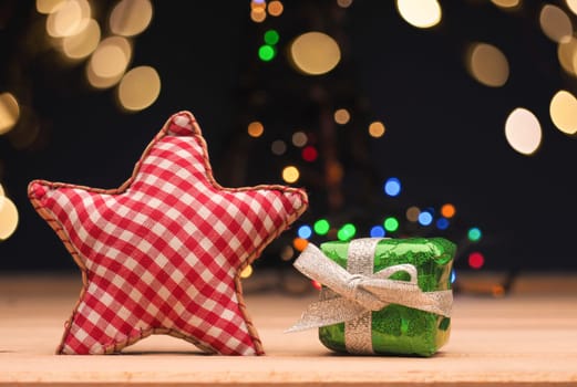 Green Christmas tgift box with a red checkered star shape on a wooden floor with Christmas lights bokeh, seasonal gift card concept