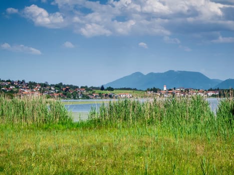 Landscape view with a view over the Hopfensee to the municipality of Hopfen am See in Bavaria in summer with a blue sky and clouds.