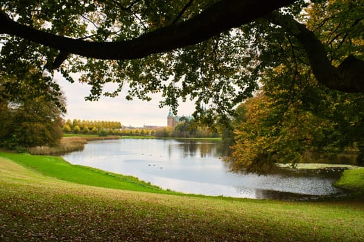 Frederiksborg Castle Park in autumn with mighty deciduous trees on the garden meadows and landscaped lake. Colorful colors of the leaves. Walk in Denmark
