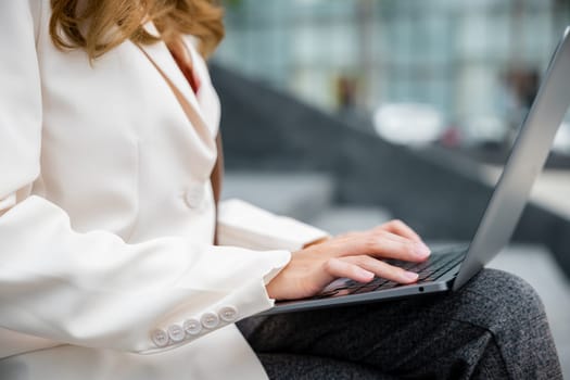 Remote working concept outside the office. Happy young Asian woman freelance smile looking laptop computer with smile while working with coffee cup while sitting on stairs outdoors in the city.