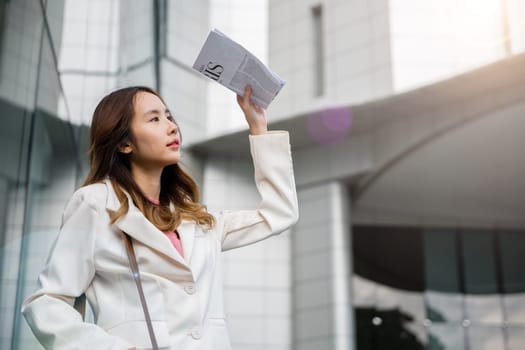 Portrait of a Young Asian woman wearing white shirt while cover the sun by news paper on the streets of downtown. She walking out the building after finish work.