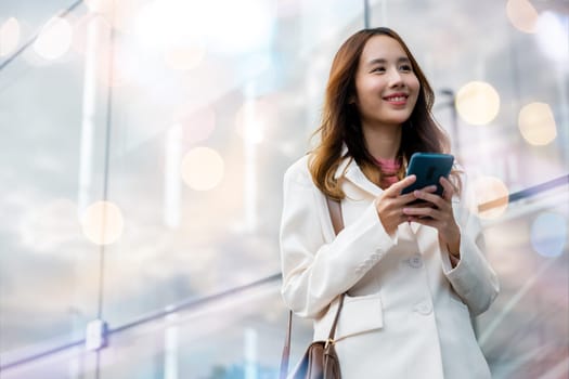 Asian businesswoman typing text on mobile phone standing outdoors street front building near office, Portrait successful business woman smiling holding smartphone using app chat online in morning