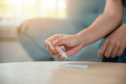 Close up woman hands using rapid antigen test kit for selftest, female four drops of liquid to perform fast coronavirus ATK self test at home in living room on sofa after lockdown and Home Isolation